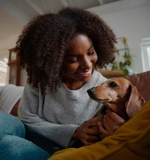 Woman sitting on a couch with a small dog, smiling.